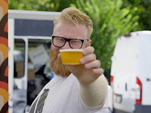 Man with beard raising a cup of beer at Barley & Smoke fundraising event